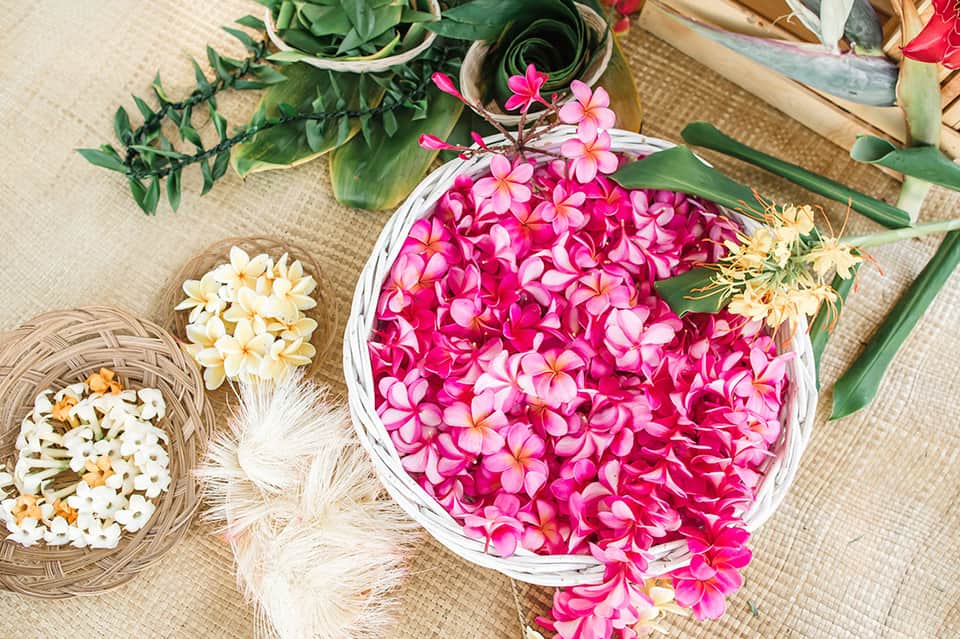 Overhead view of pink and white flowers arranged in baskets on woven mat