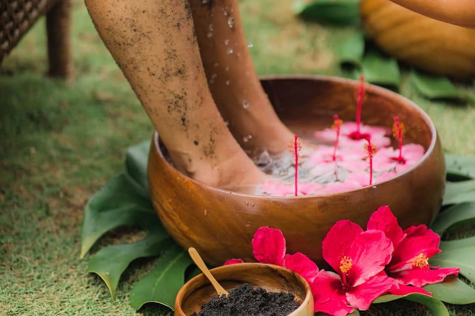 Feet soaking in wooden bowl with pink flower petals and spa setting