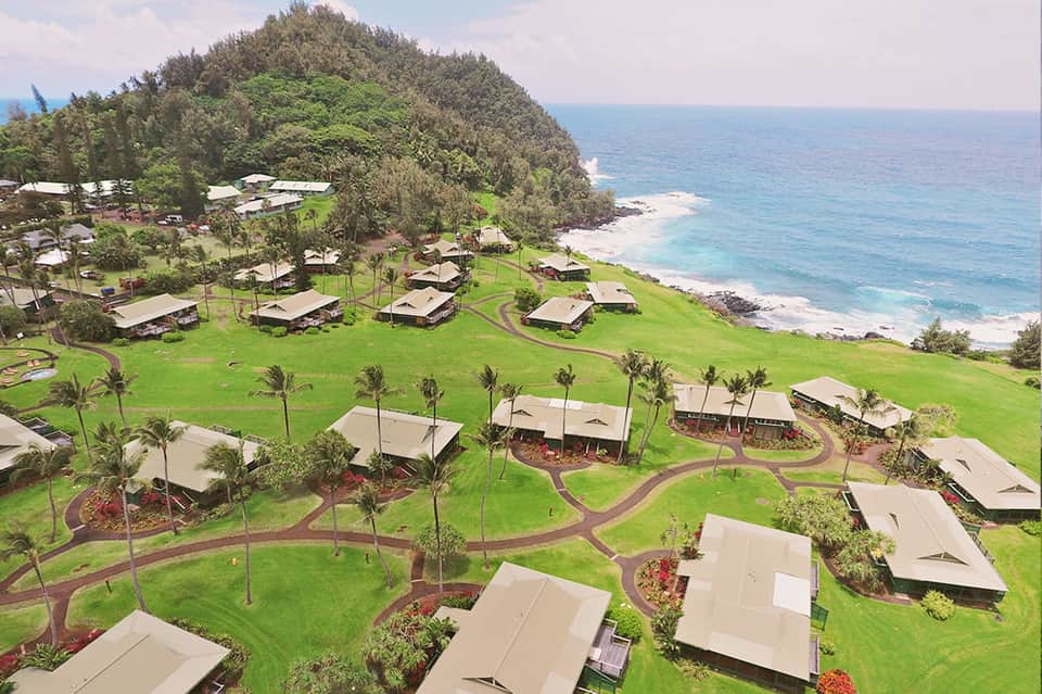 Aerial view of beachfront resort with white tent cabanas scattered across green lawn beside rocky coastline
