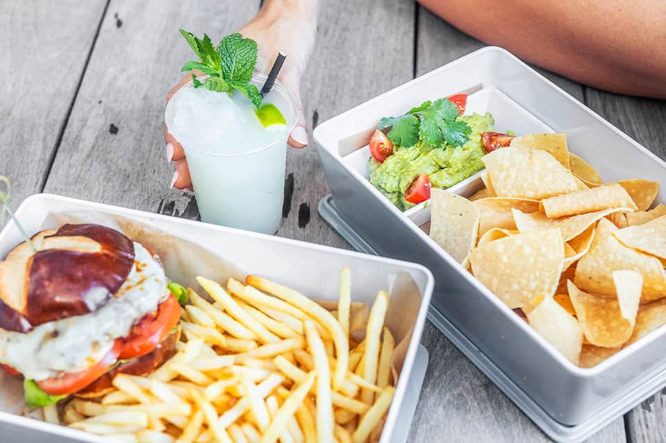 Overhead view of food and beverage spread including sandwich, fries, guacamole, chips, and mint cocktail