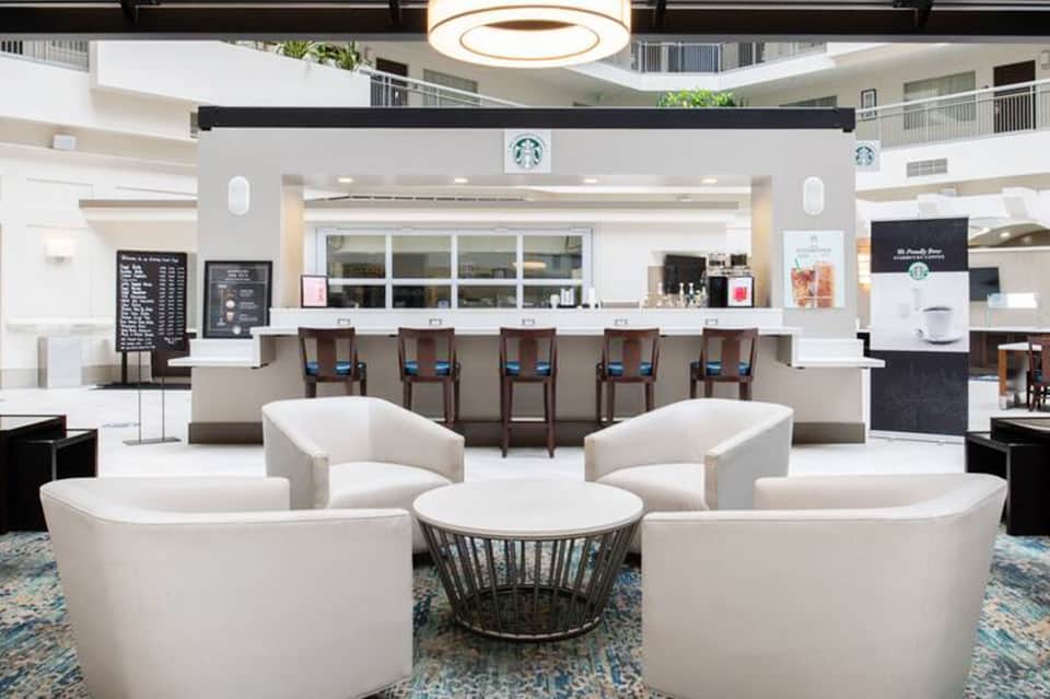 Modern hotel lobby with white curved seating, Starbucks counter, and circular ceiling light