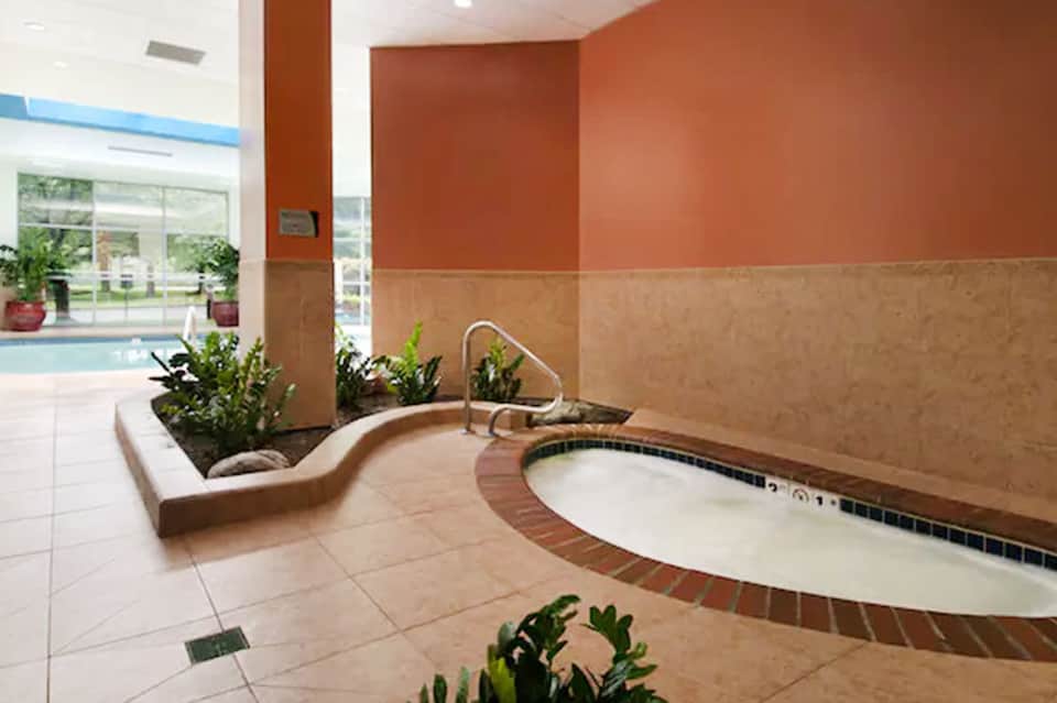 Spa interior with whirlpool tub, orange accent walls, plants, and view to indoor pool area