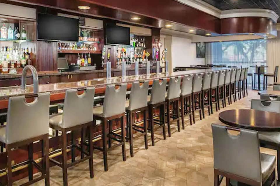 Upscale bar with long countertop seating, dark wood cabinetry, multiple TV screens, and professional liquor display