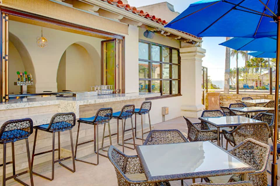 Outdoor patio bar with blue umbrellas, woven chairs, and ocean views at a coastal resort