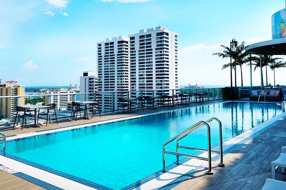 Expansive blue resort pool with lounge chairs and high-rise hotel building overlooking ocean