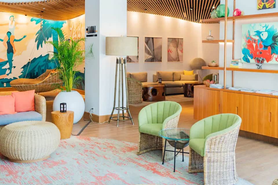 Colorful modern lounge with vibrant wall art, woven chairs, wooden shelving, and tropical plants