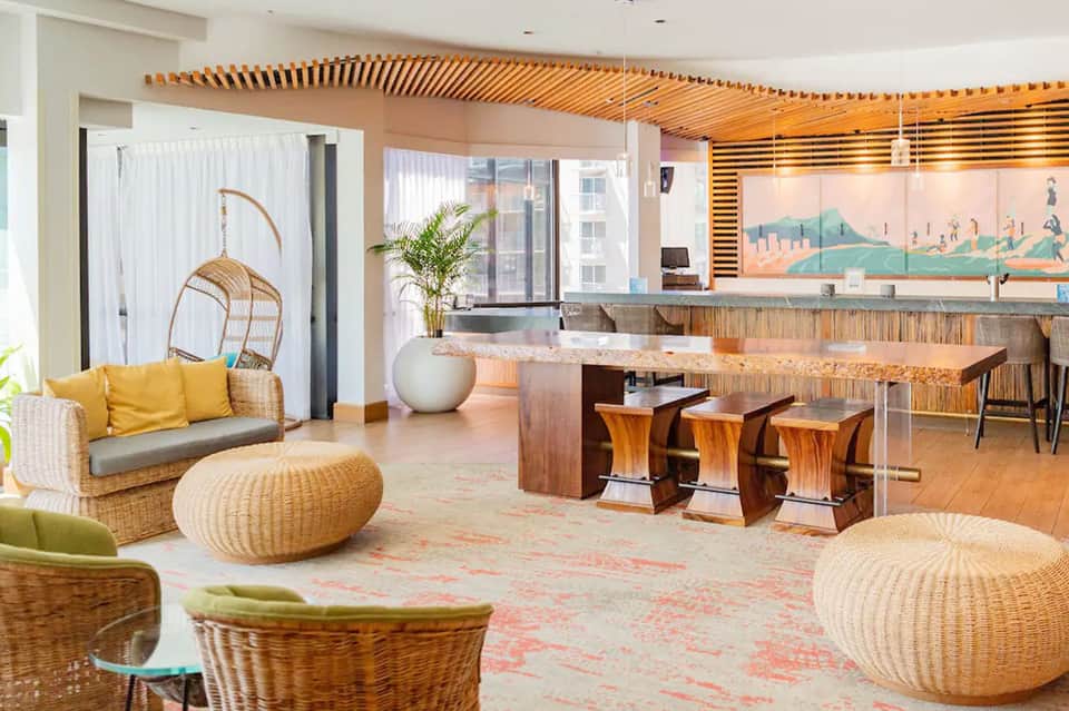 Modern resort lobby with woven seating, wooden bar counter, and contemporary coastal design elements
