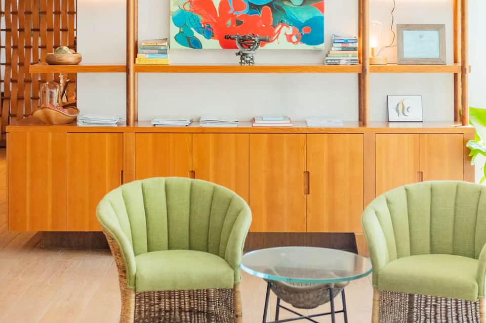 Mid-century modern lounge with wooden shelving, green armchairs, and colorful abstract artwork