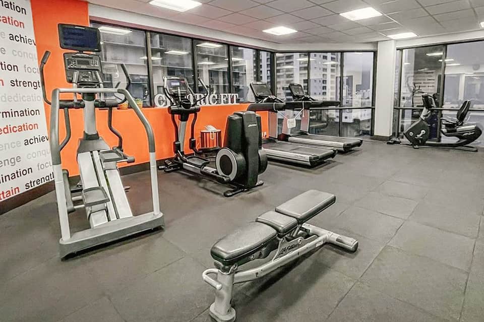 Modern fitness center with orange accents, cardio equipment, and city window views