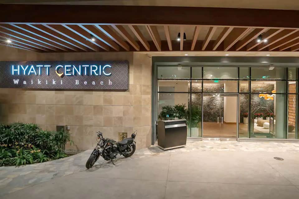 Hotel entrance with illuminated Hyatt Centric Waikiki Beach neon sign and glass doors