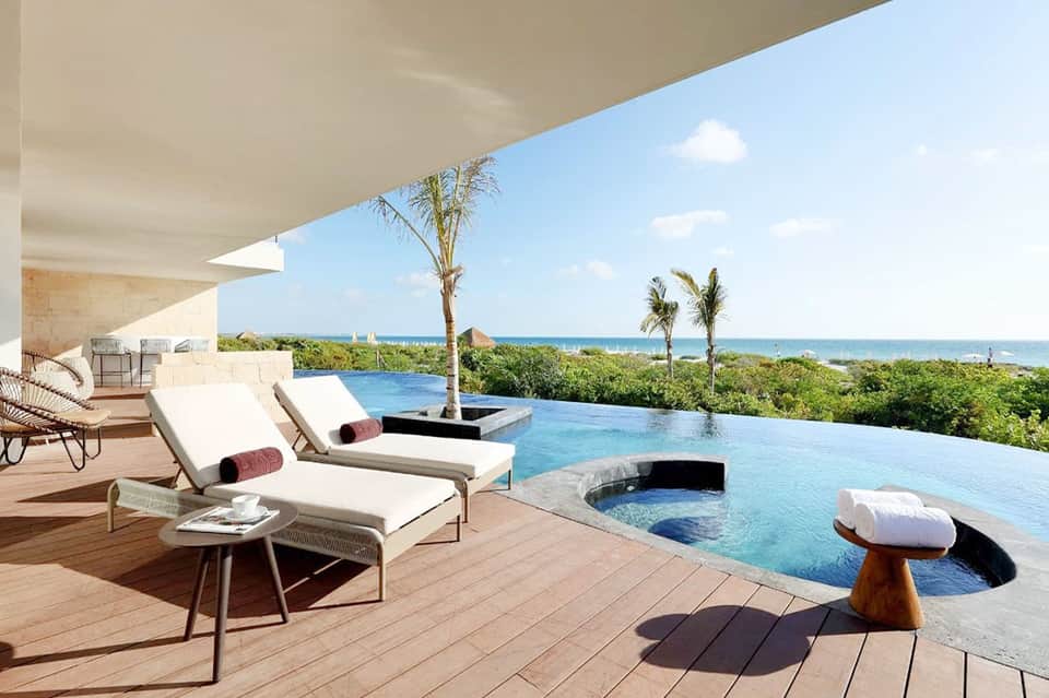 Infinity pool overlooking ocean with palm trees, modern loungers, and coastal landscape