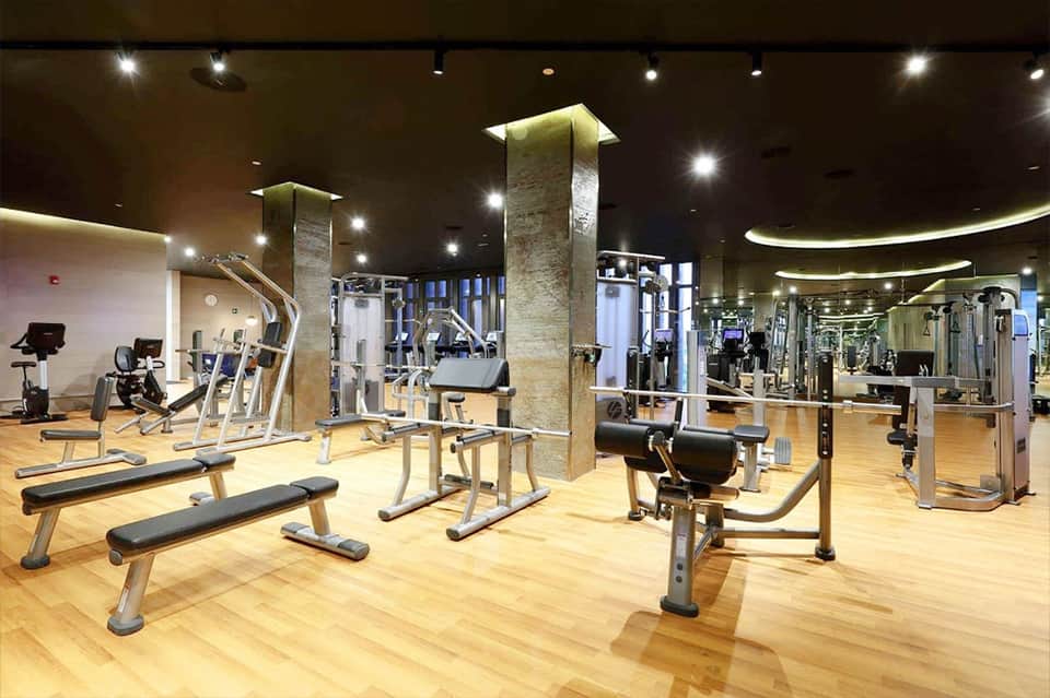 Modern gym interior with exercise equipment, mirrors, stone columns, and bright lighting
