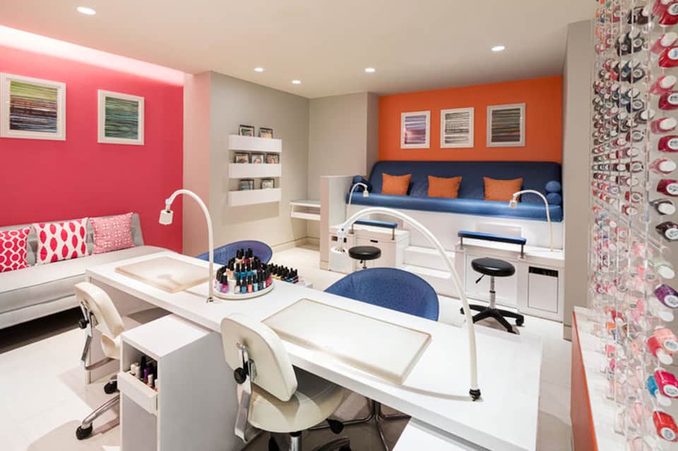 Colorful spa room with manicure stations, pink walls, orange accents, and beds for treatments
