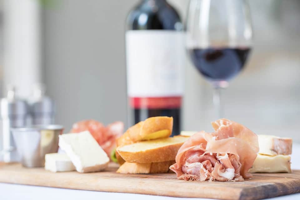 Charcuterie board with cured meats, cheese, and bread beside red wine glass