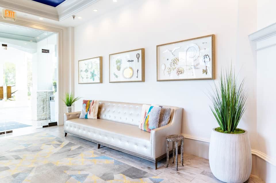 Modern hotel lobby with cream sofa, framed coastal artwork, potted plant, and bright natural lighting