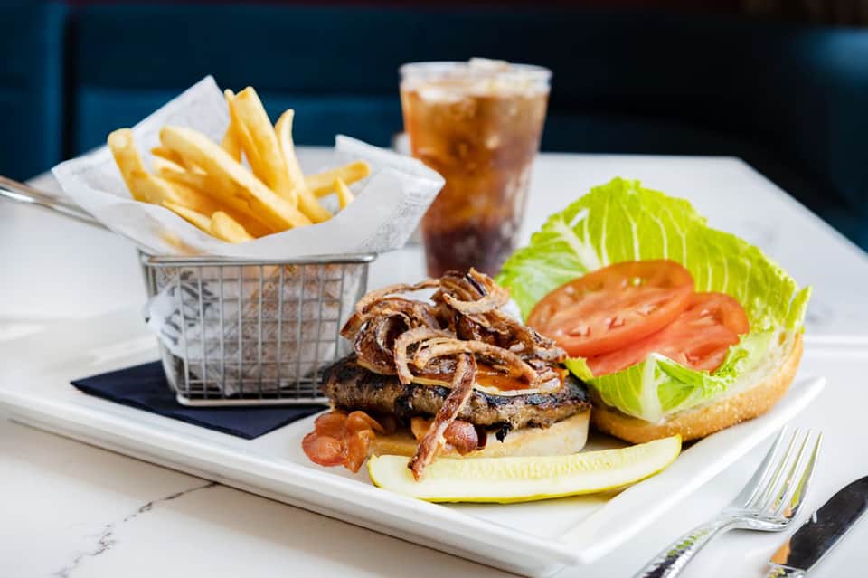 Gourmet burger with fries and beverage on white plate at resort restaurant