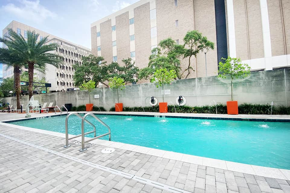 Resort swimming pool with lounge chairs and modern building with orange accent walls and palm trees