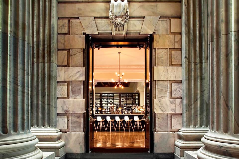 Elegant bar entrance framed by classical stone columns with art deco styling and warm interior lighting