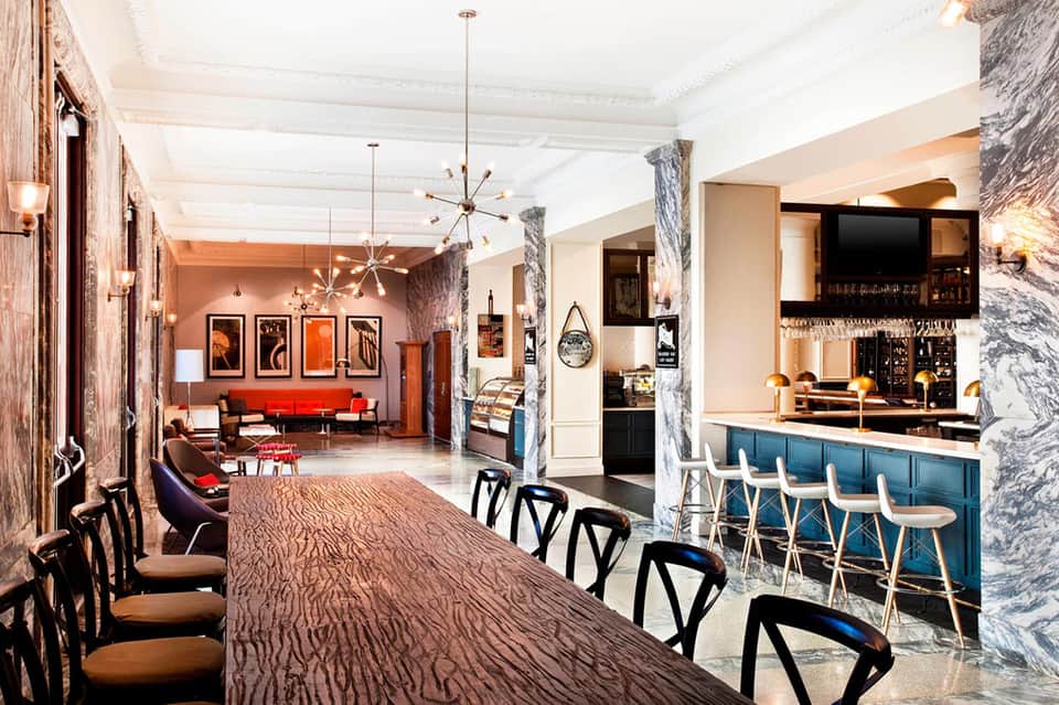 Hotel lobby and bar area with red sofa, marble columns, and modern chandelier