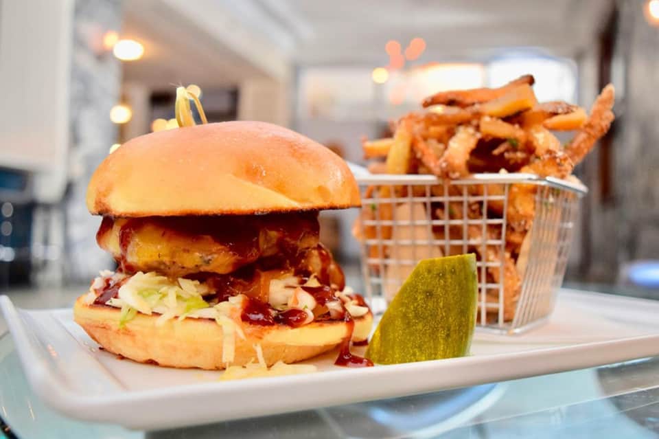 Gourmet burger with crispy fried chicken patty, coleslaw, and sweet potato fries in basket