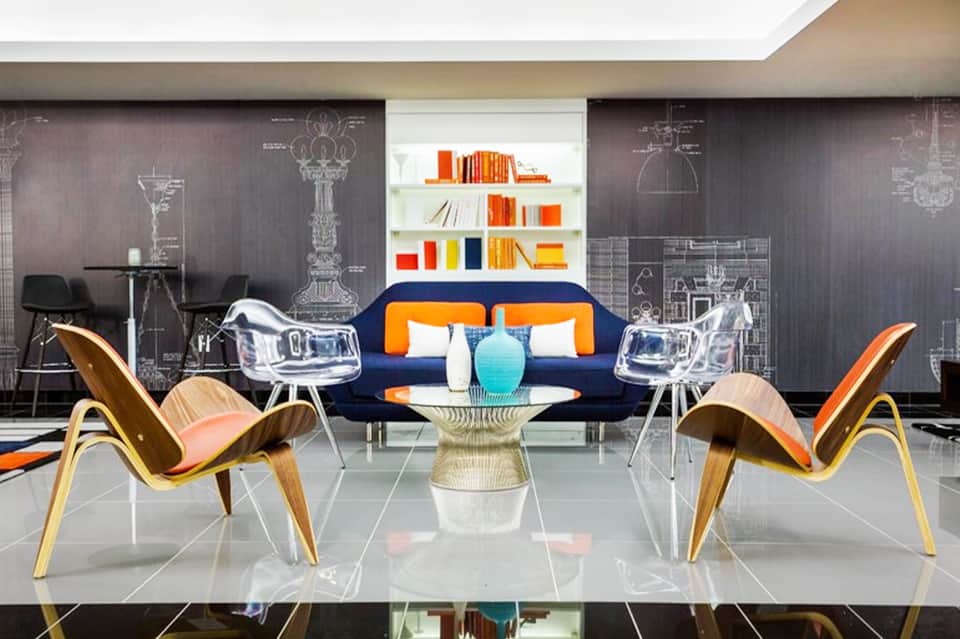 Contemporary lobby with bold navy sofa, orange accent chairs, geometric wall art, and colorful bookshelf