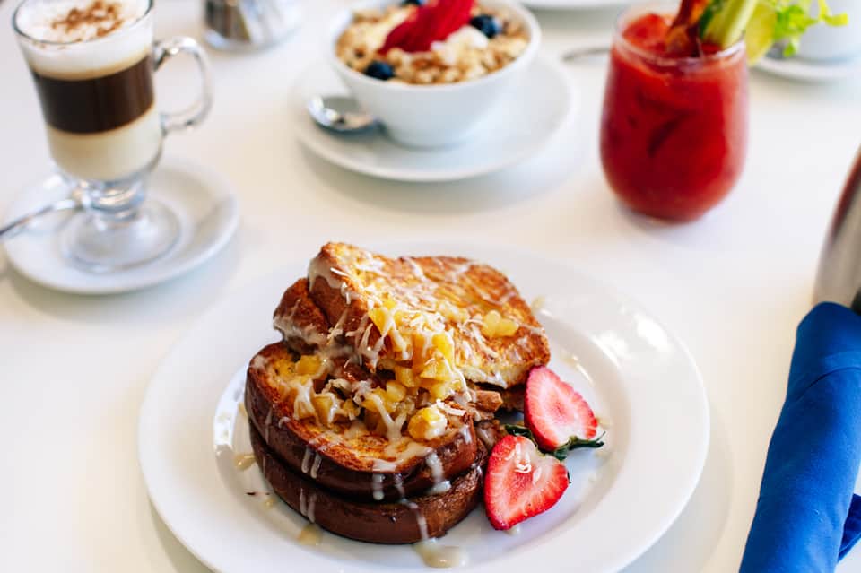 Gourmet breakfast plate with French toast, berries, coffee, and fresh juice on white table