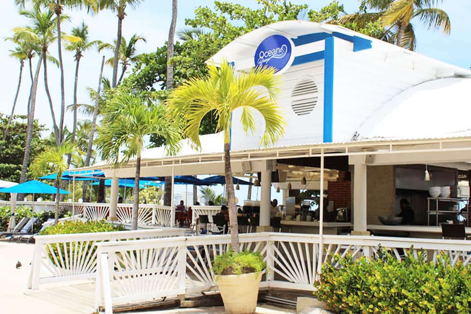 Oceanfront café with white railings, palm trees, and blue-and-white branded building structure