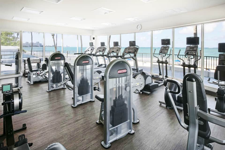 Bright fitness center with cardio equipment and floor-to-ceiling windows overlooking the ocean