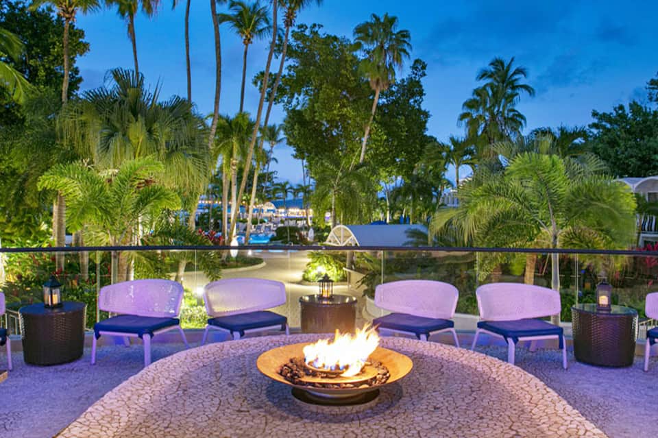 Resort fire pit seating area with purple chairs, palm trees, and lagoon view at dusk