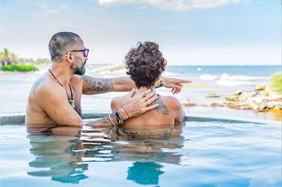 Couple relaxing in infinity pool overlooking ocean and beach landscape, tropical setting