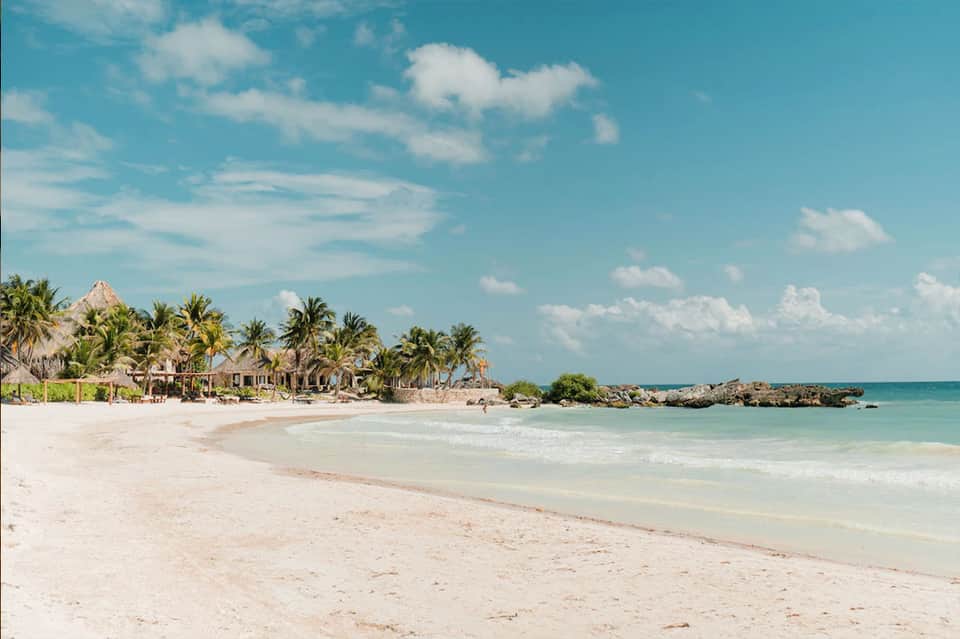 Tropical beach resort with white sand, turquoise water, palm trees, and thatched-roof structures