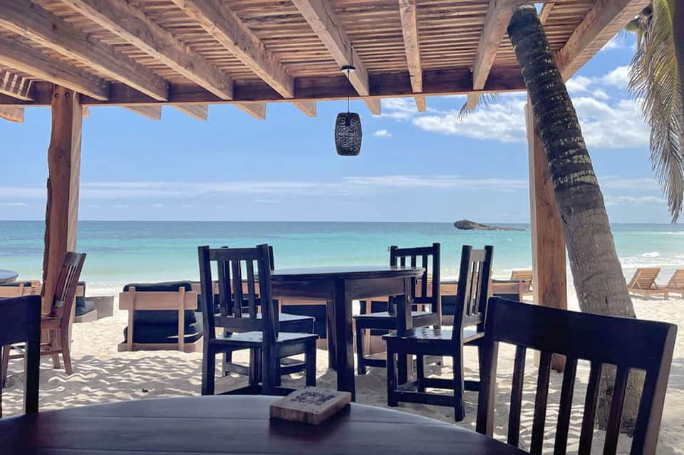 Beachfront dining area under wooden pergola with ocean view and black chairs