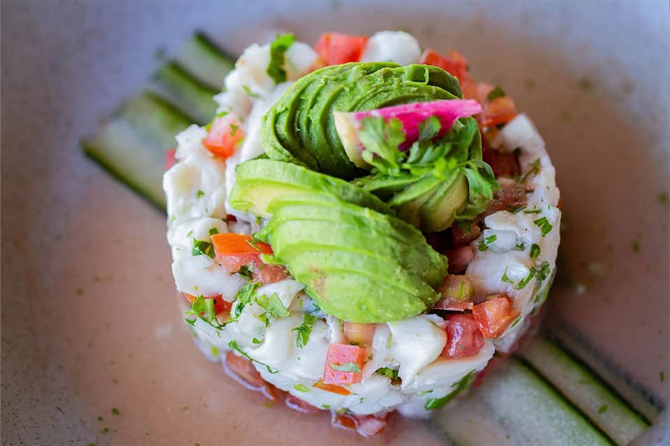 Gourmet sushi roll topped with sliced avocado, fresh vegetables, and garnish on wooden surface