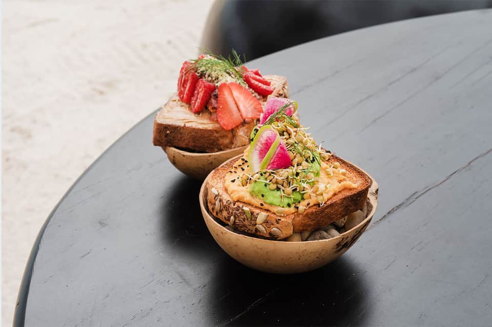 Two gourmet appetizers served in bronze bowls with fresh berries and microgreens on dark table