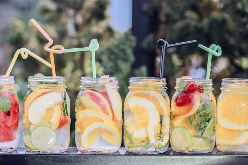 Colorful infused water drinks in mason jars with decorative straws on outdoor table