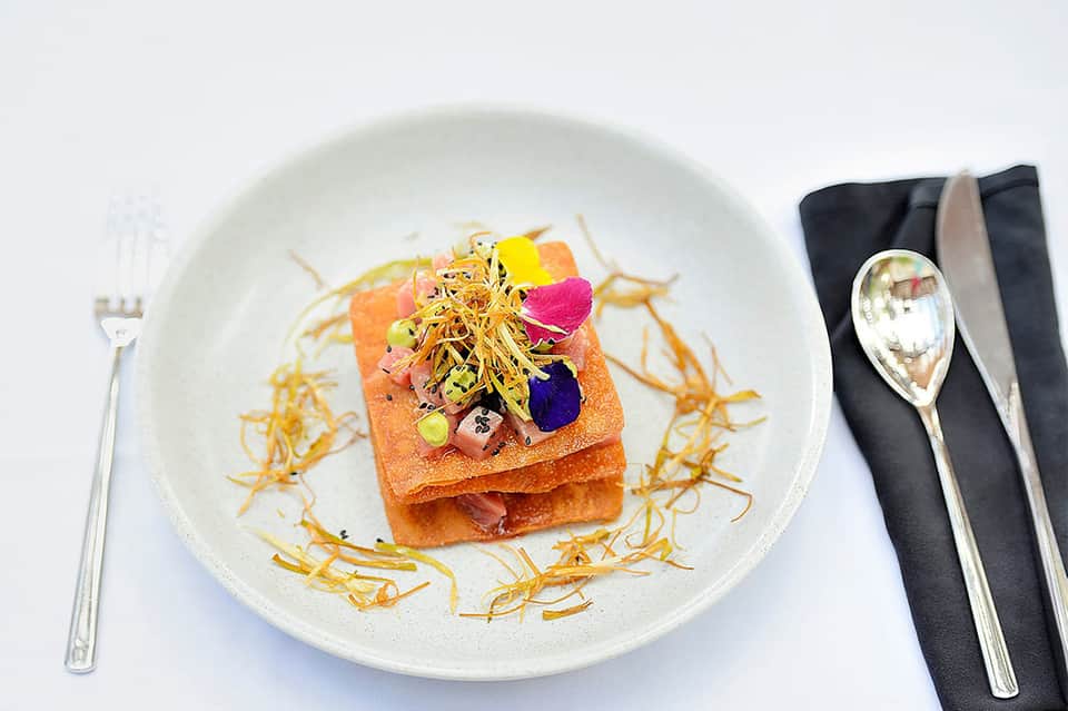 Artfully plated gourmet dish with colorful microgreens on white plate with gold accents