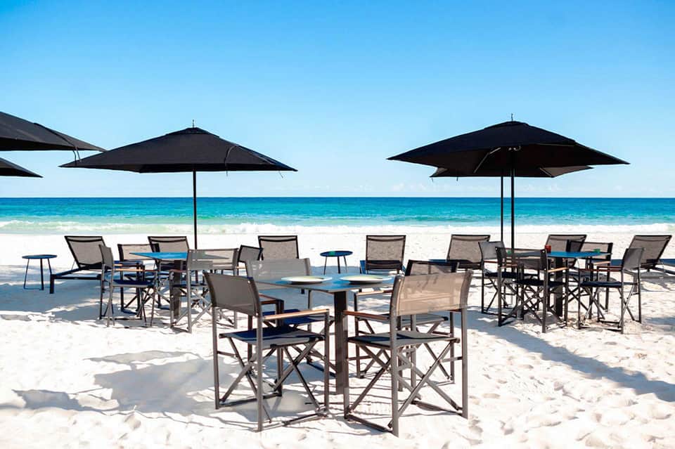 Beach dining area with multiple black umbrellas, chairs, and ocean view