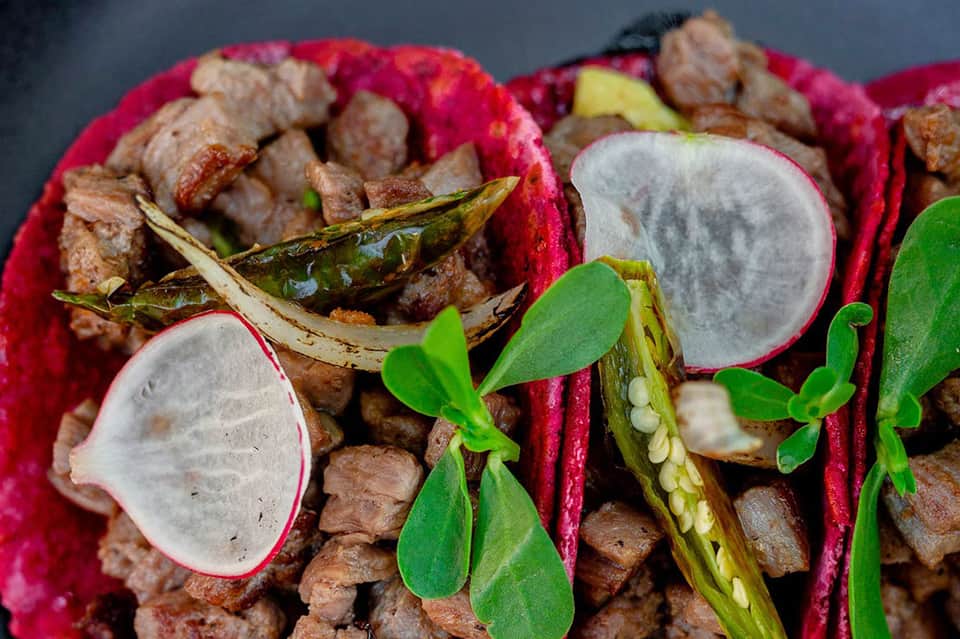 Close-up of dragon fruit cut in half with green leaves and meat cubes on pink background