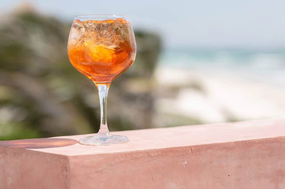 Amber cocktail with ice in wine glass on terrace railing with blurred beach background