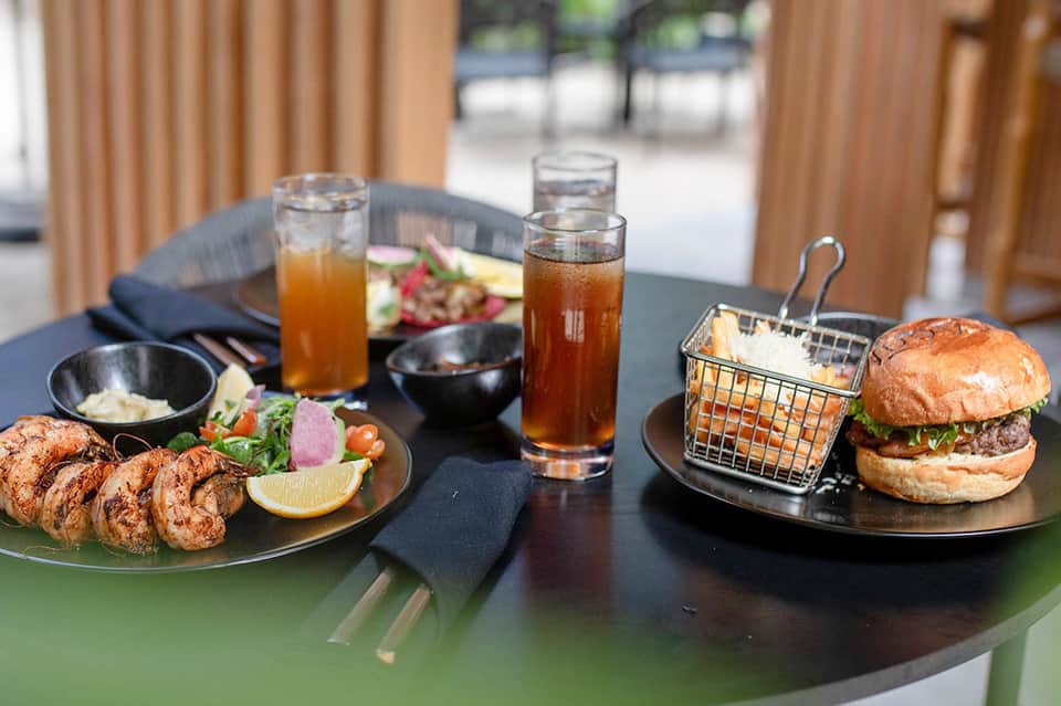 Upscale outdoor dining table with shrimp appetizer, burger, and beverages