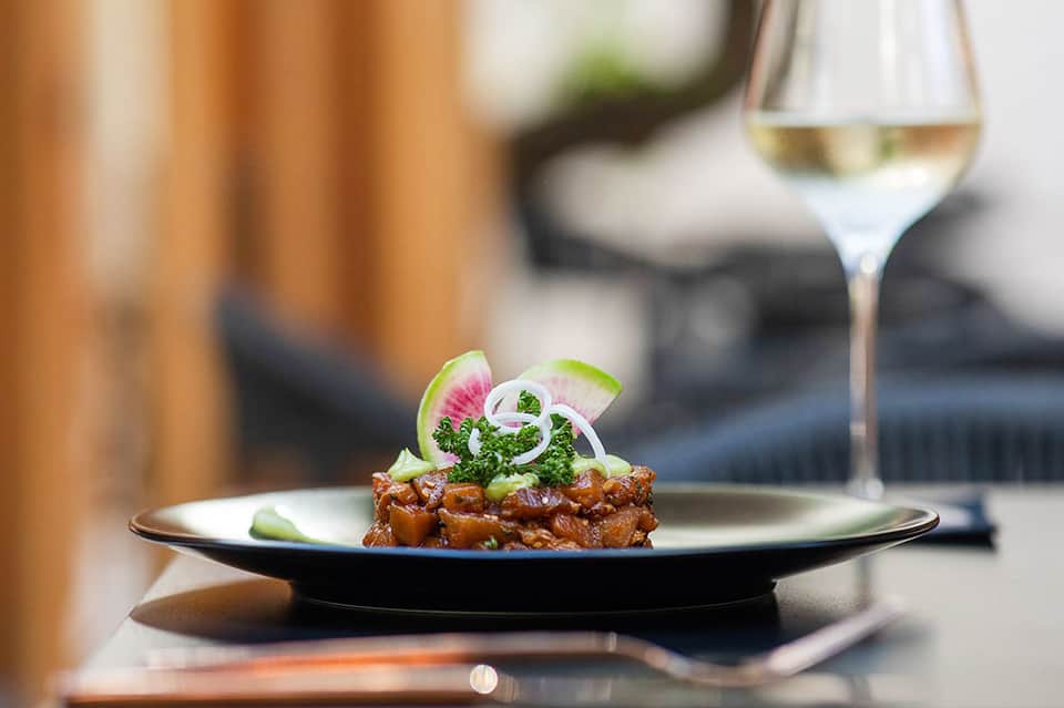 Plated appetizer with microgreens and white wine glass on outdoor dining table