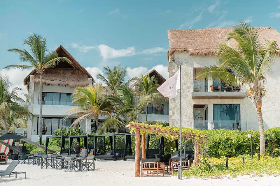 Modern beachfront villas with thatched roofs, palm trees, and sand beach access