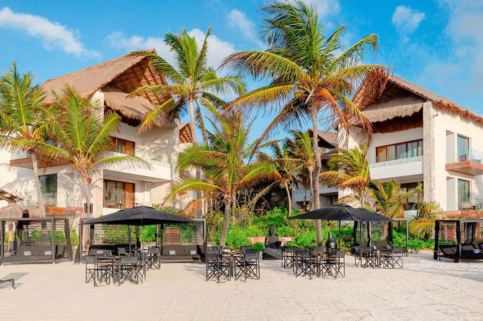 Beachfront resort with thatched-roof bungalows, palm trees, and dining pavilions on sandy beach