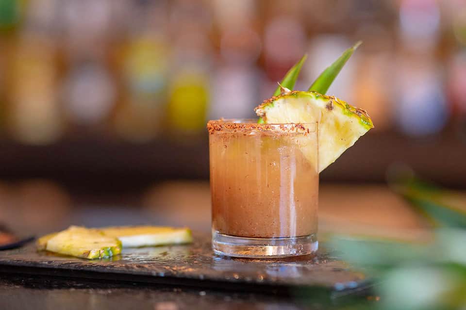 Tropical cocktail with pineapple garnish and cinnamon rim on dark surface
