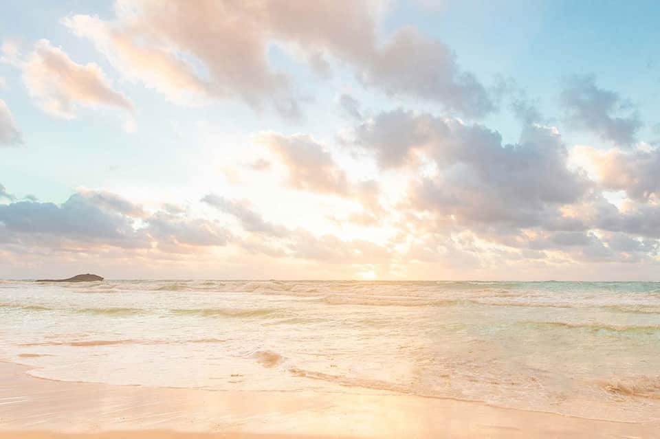 Serene beach at sunrise with calm waves, sandy shore, and soft clouds over ocean