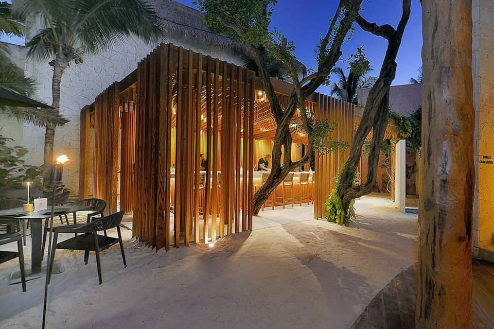 Illuminated wooden pavilion structure in courtyard at dusk with palm trees