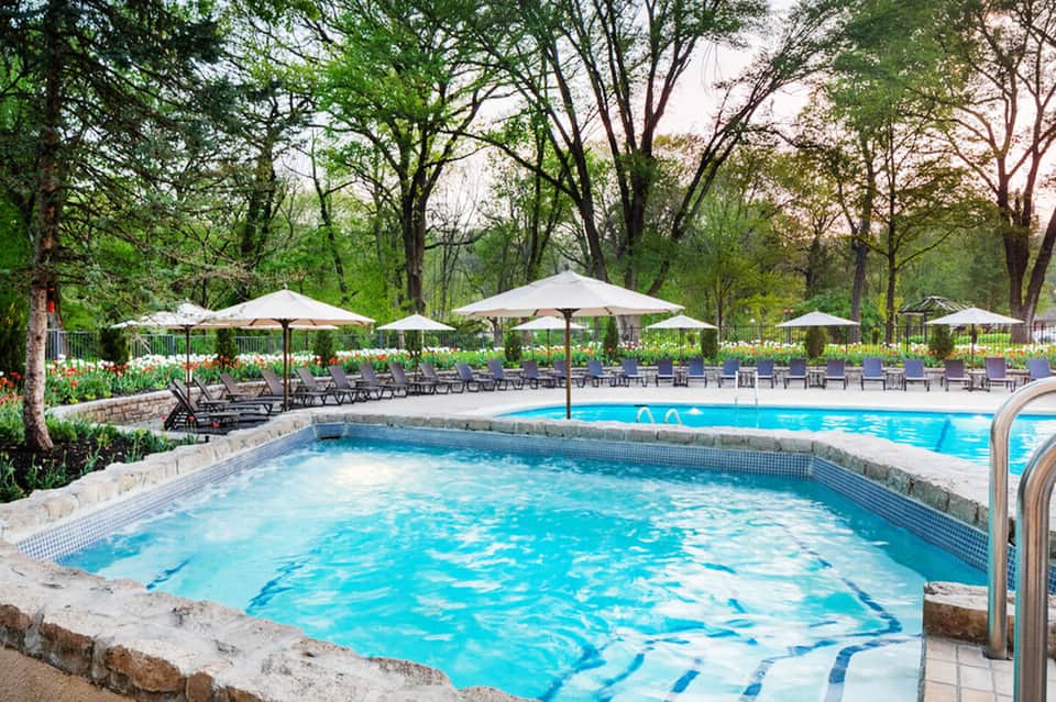 Resort hot tub surrounded by lounge chairs and white umbrellas in a wooded garden setting