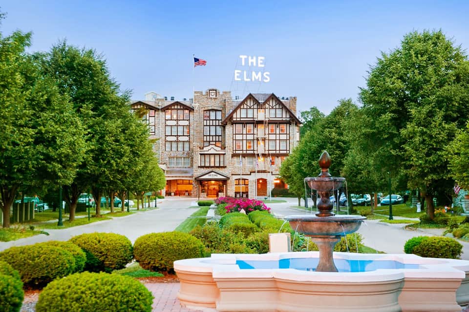 The Elms historic Tudor-style building with stone facade, manicured gardens, fountain, and tree-lined courtyard approach