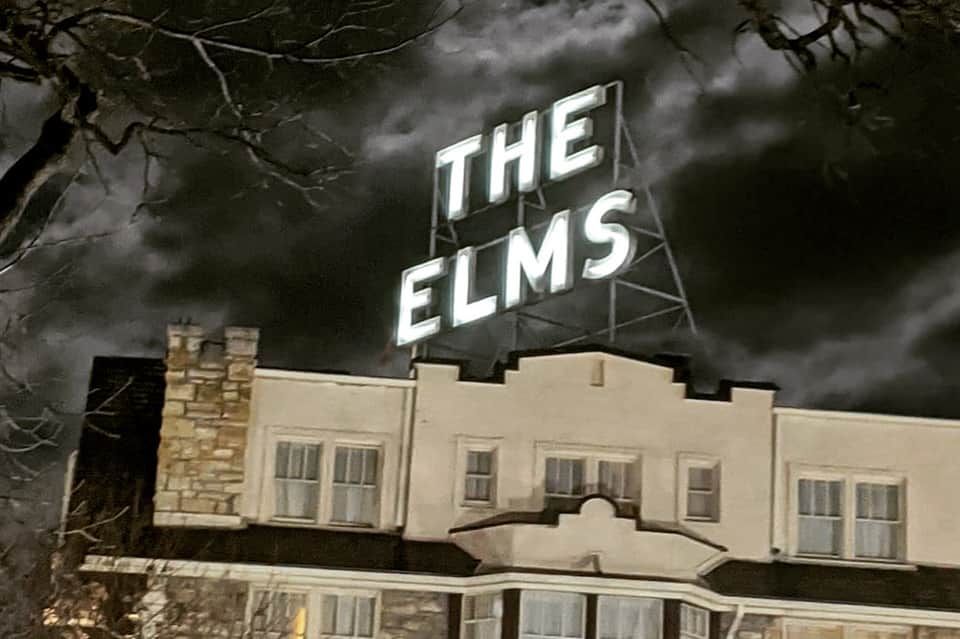 The Elms vintage neon sign on historic building facade against stormy sky