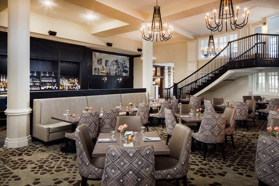 Upscale restaurant interior with elegant chandeliers, booth seating, bar area, and decorative staircase